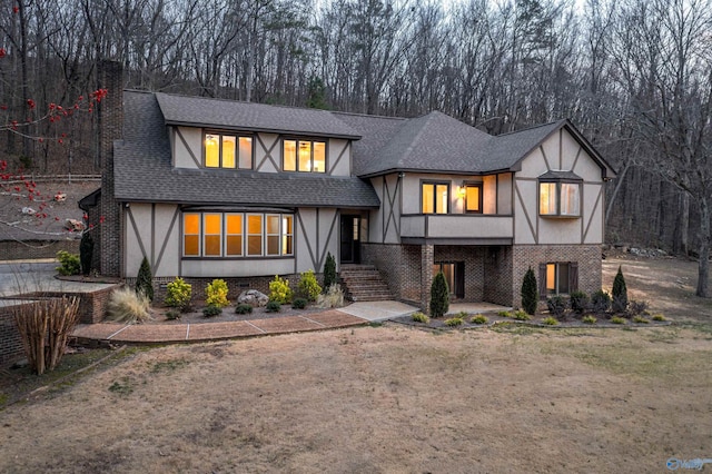 tudor home with a shingled roof, stucco siding, and brick siding