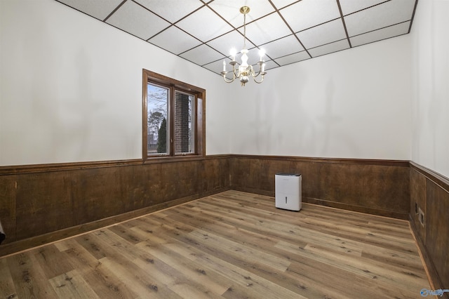 unfurnished dining area featuring wood walls, a chandelier, wainscoting, and wood finished floors