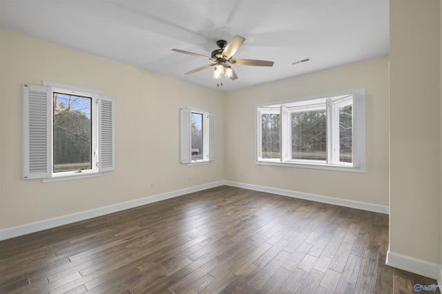 spare room featuring baseboards, ceiling fan, visible vents, and dark wood finished floors
