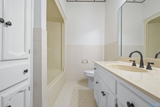 bathroom featuring a wainscoted wall, toilet, vanity, tile patterned flooring, and tile walls