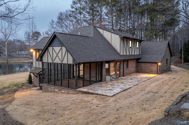 back of house featuring a sunroom, brick siding, roof with shingles, stucco siding, and a patio area