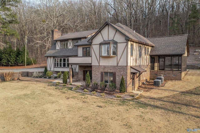 tudor-style house featuring a front yard, a chimney, stucco siding, brick siding, and a shingled roof