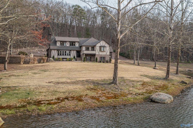 view of front facade featuring a water view, a shingled roof, and a front lawn
