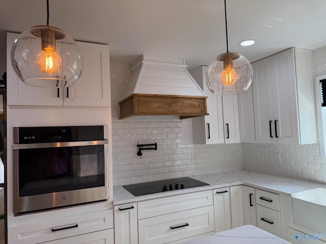 kitchen featuring custom range hood, black electric cooktop, decorative light fixtures, white cabinets, and oven