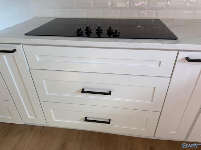 interior details with white cabinetry, light stone countertops, black electric cooktop, and light wood-type flooring