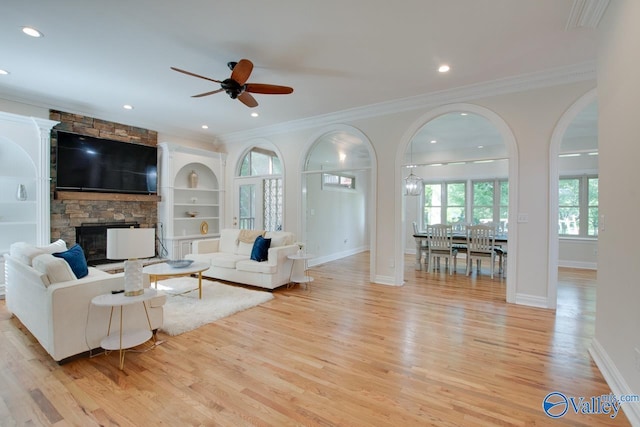 living area featuring a fireplace, ceiling fan, ornamental molding, and light wood finished floors