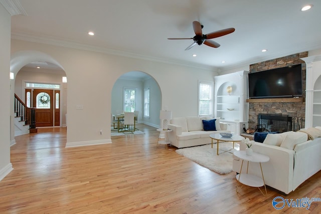 living room featuring ceiling fan, a fireplace, arched walkways, light wood-style flooring, and recessed lighting