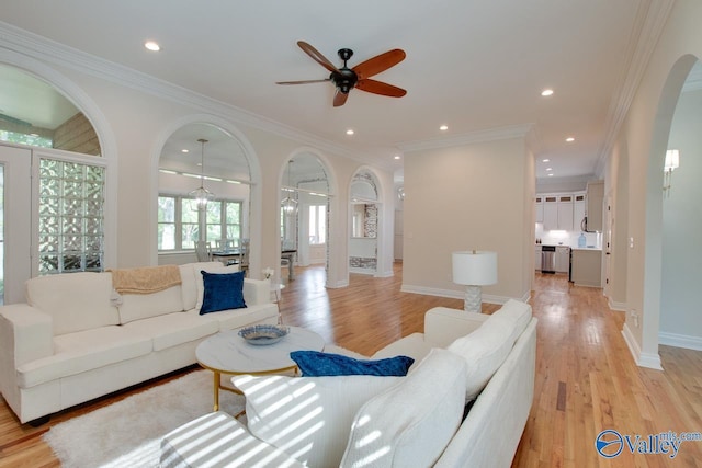 living area with crown molding, arched walkways, ceiling fan, and light wood finished floors