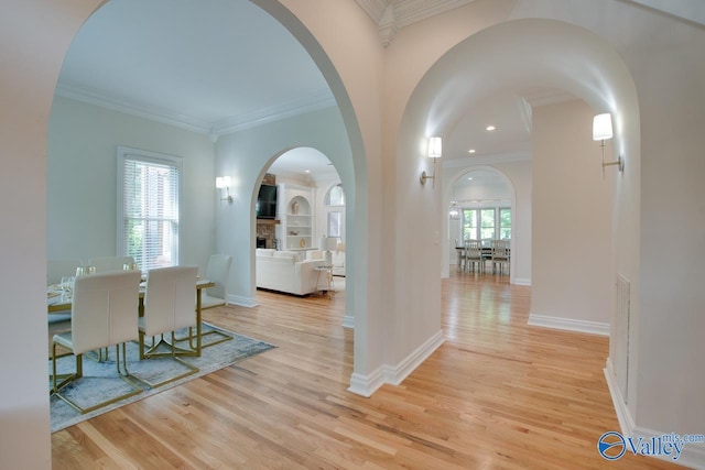 corridor featuring light wood finished floors, arched walkways, recessed lighting, baseboards, and ornamental molding