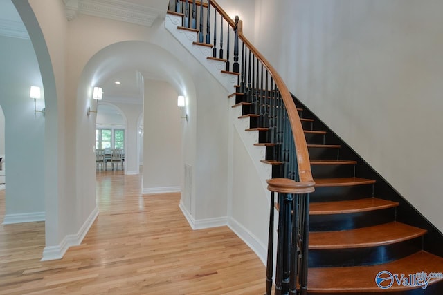 stairway featuring crown molding, arched walkways, a high ceiling, and wood finished floors