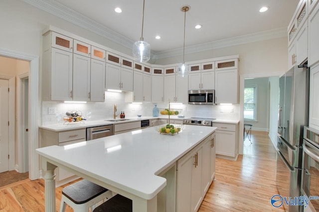 kitchen featuring a kitchen island, light countertops, a sink, appliances with stainless steel finishes, and backsplash