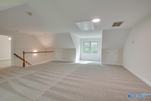 additional living space with light carpet, visible vents, attic access, baseboards, and vaulted ceiling