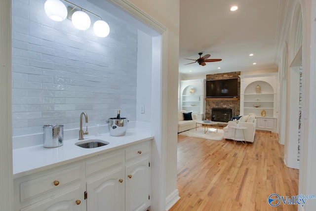 bar featuring ceiling fan, a stone fireplace, tasteful backsplash, a sink, and light wood-style floors