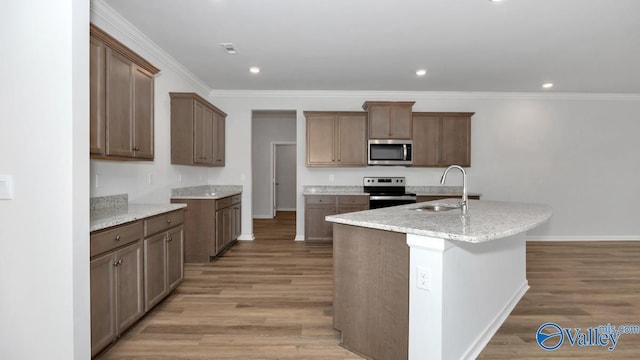 kitchen with stainless steel appliances, sink, light hardwood / wood-style floors, and a kitchen island with sink