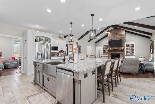 kitchen featuring a breakfast bar, stainless steel appliances, hanging light fixtures, open floor plan, and a large island with sink