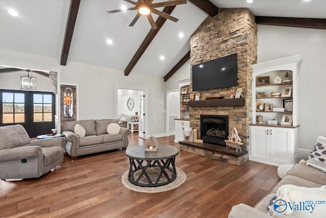 living room with visible vents, wood finished floors, a stone fireplace, high vaulted ceiling, and beam ceiling