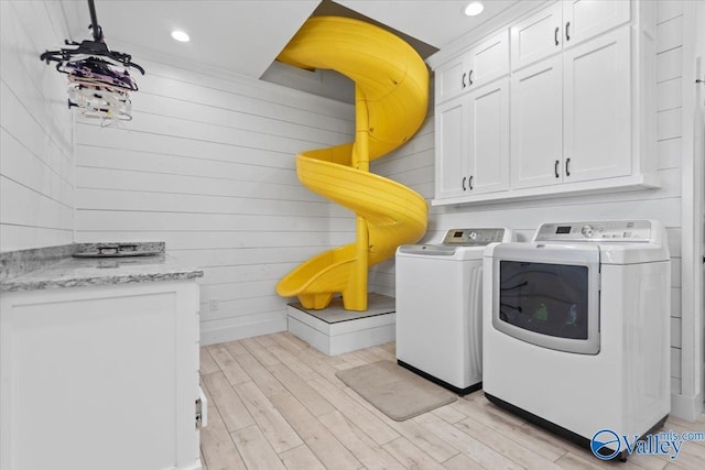 clothes washing area with recessed lighting, wooden walls, light wood-type flooring, independent washer and dryer, and cabinet space