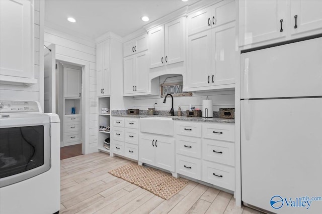 kitchen with washer / clothes dryer, freestanding refrigerator, white cabinetry, light stone countertops, and light wood-type flooring