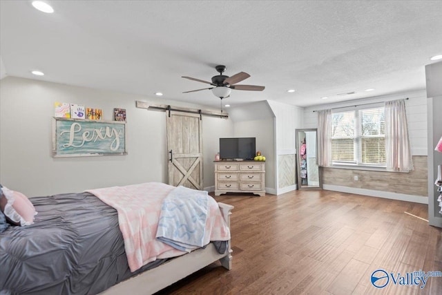 bedroom with a barn door, a textured ceiling, wood finished floors, and recessed lighting