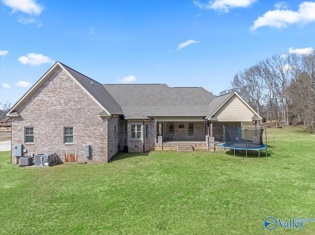 back of house with a trampoline, brick siding, a yard, and central AC unit