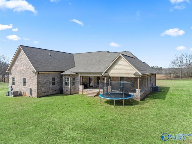 rear view of house featuring a trampoline, brick siding, crawl space, and a lawn