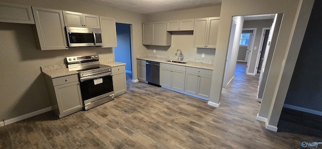 kitchen with appliances with stainless steel finishes, a textured ceiling, dark wood-type flooring, and sink