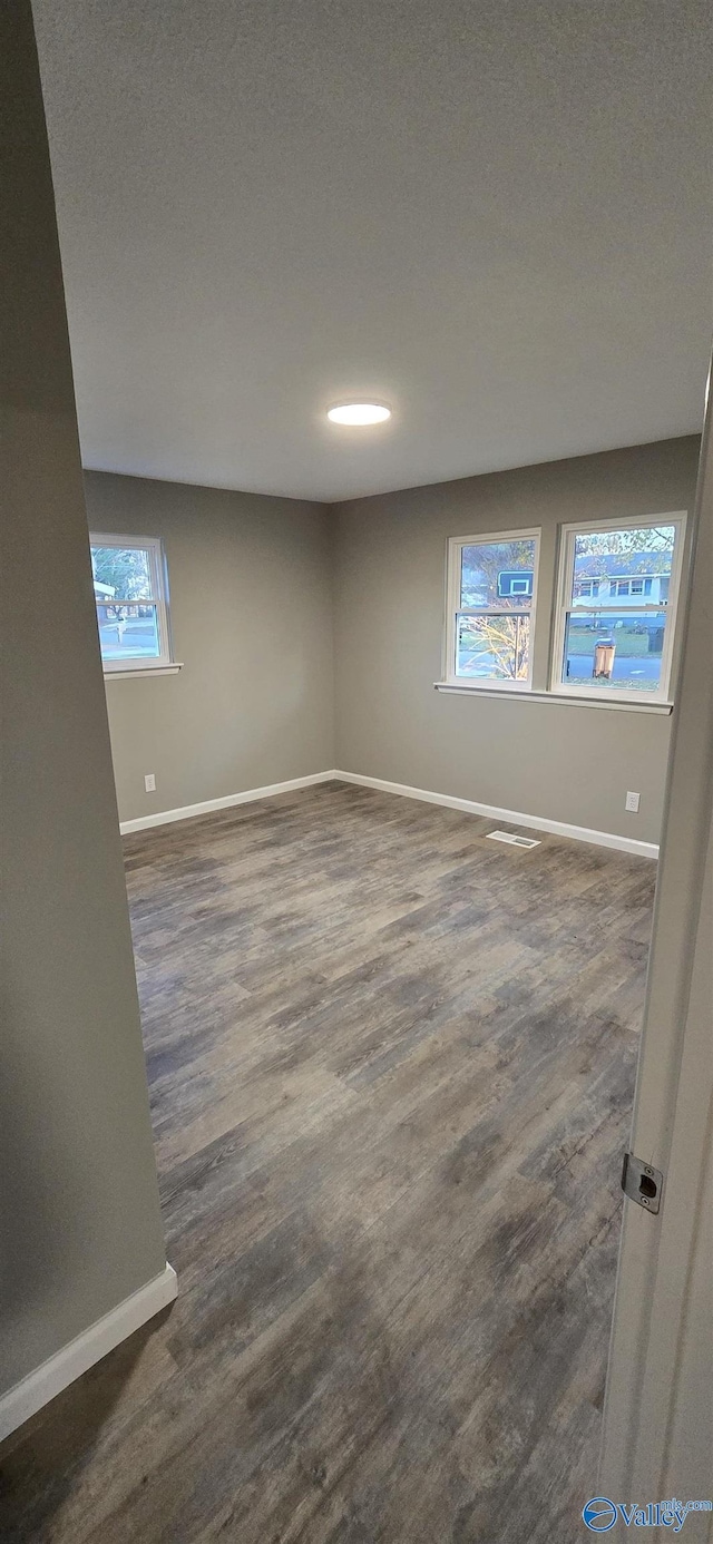 empty room with plenty of natural light, dark hardwood / wood-style flooring, and a textured ceiling