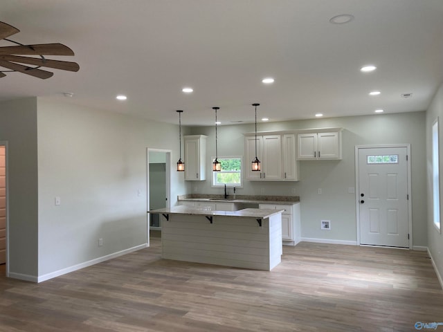 kitchen featuring a kitchen island, light stone countertops, light hardwood / wood-style flooring, and white cabinets