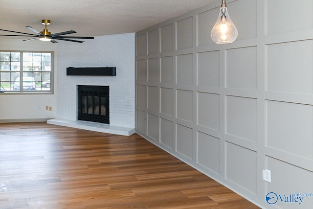 unfurnished living room with hardwood / wood-style floors, a textured ceiling, a brick fireplace, and ceiling fan