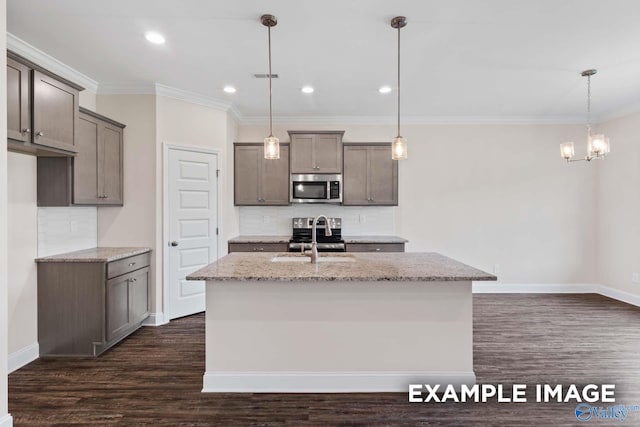 kitchen with light stone counters, appliances with stainless steel finishes, hanging light fixtures, and an island with sink