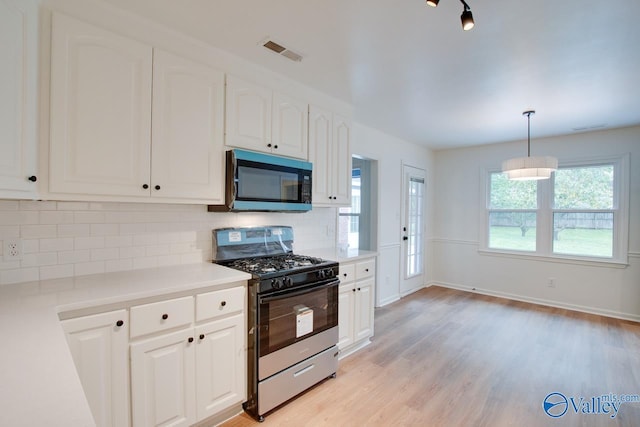 kitchen featuring decorative backsplash, stainless steel microwave, light wood-style floors, visible vents, and range with gas stovetop