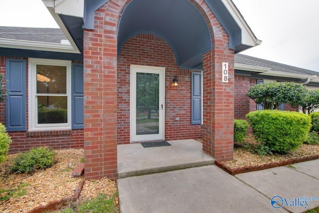 entrance to property featuring roof with shingles and brick siding
