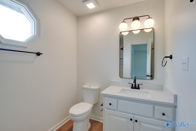 bathroom with toilet, vanity, wood finished floors, and baseboards