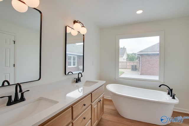full bath with a freestanding tub, wood finished floors, double vanity, and a sink