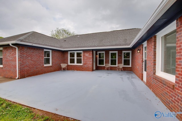 back of property with brick siding, a shingled roof, and a patio area
