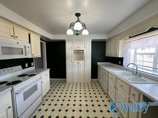 kitchen with sink, hanging light fixtures, a notable chandelier, white appliances, and cream cabinetry