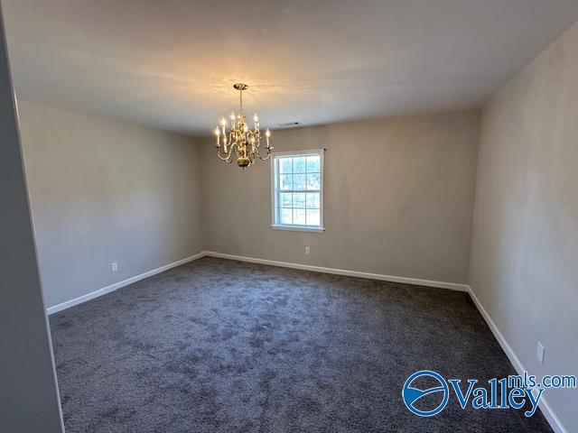 unfurnished room featuring dark colored carpet and a chandelier