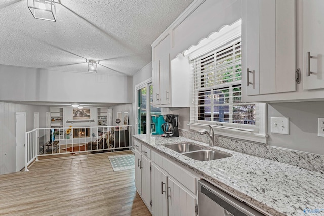 kitchen featuring white cabinets, a sink, light wood-type flooring, dishwasher, and a lit fireplace