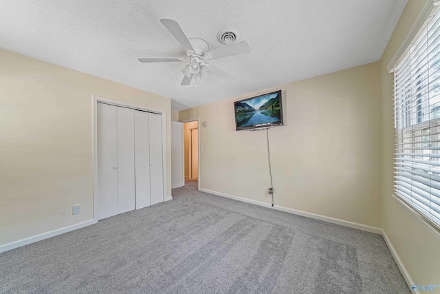 unfurnished bedroom featuring carpet, a closet, visible vents, a textured ceiling, and baseboards