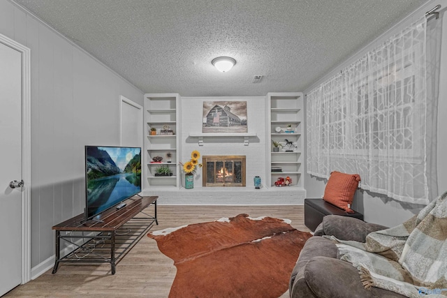 living area featuring a textured ceiling, built in shelves, a fireplace, and wood finished floors