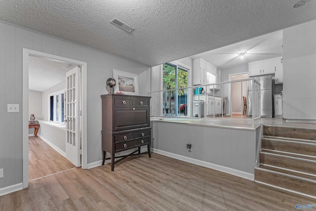 interior space with visible vents, wood finished floors, freestanding refrigerator, a textured ceiling, and white cabinetry