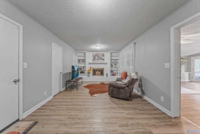 sitting room with baseboards, a glass covered fireplace, wood finished floors, a textured ceiling, and built in shelves