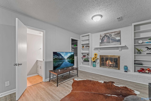 living room with a textured ceiling, a fireplace, wood finished floors, and built in features