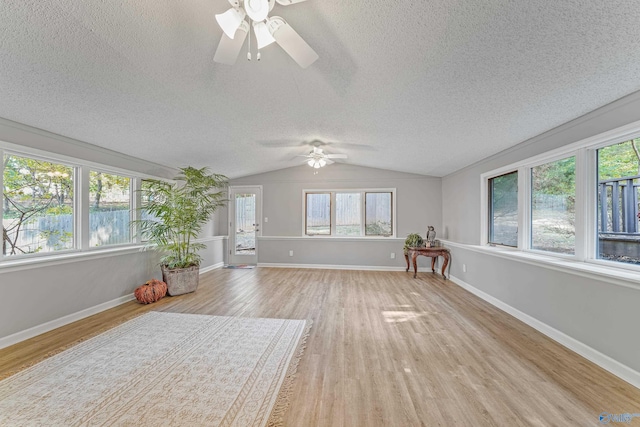 interior space featuring light wood-type flooring, vaulted ceiling, a textured ceiling, and baseboards