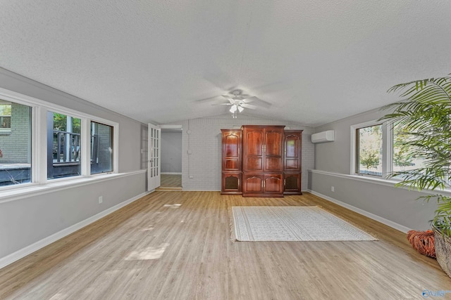 unfurnished living room with light wood-style floors, an AC wall unit, vaulted ceiling, a textured ceiling, and baseboards