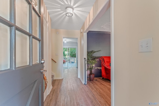 hallway with baseboards, a textured ceiling, and light wood finished floors