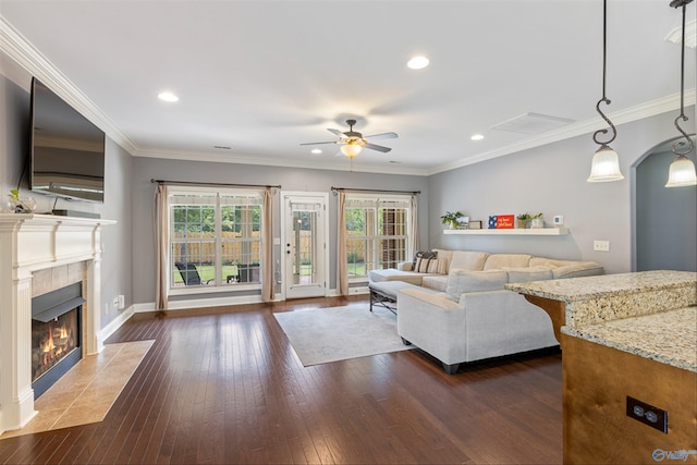 living room featuring dark hardwood / wood-style flooring, a tiled fireplace, crown molding, and ceiling fan