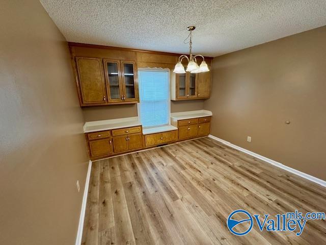 unfurnished dining area featuring a chandelier, a textured ceiling, and light wood-type flooring