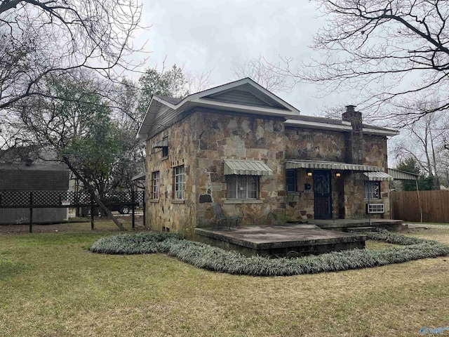 rear view of property with stone siding, a lawn, a chimney, and fence