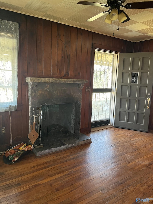 unfurnished living room with wood-type flooring, wooden walls, and ceiling fan